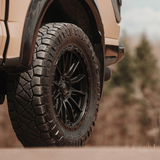Close-up of a vehicle tire with off-road tread pattern on a blurred natural background